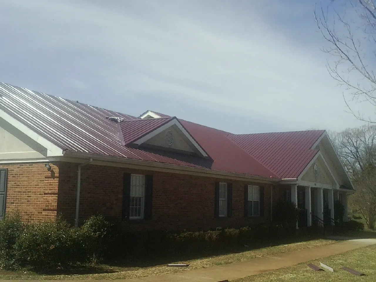 Red metal roof with gabled entries on a long brick building, from a Hail Damage Roof Repair job in Anatone