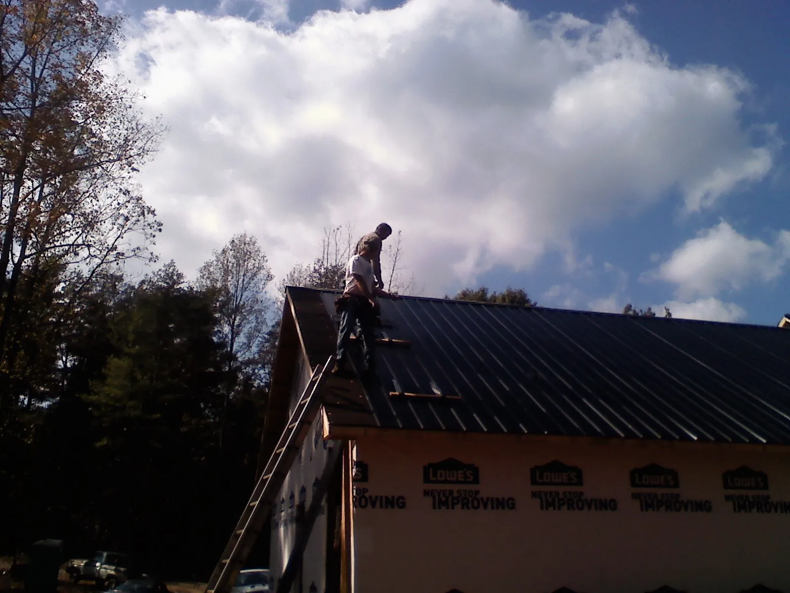 Roofer fastening dark metal panels high against a cloudy sky, from a Roof Inspection job in Anatone